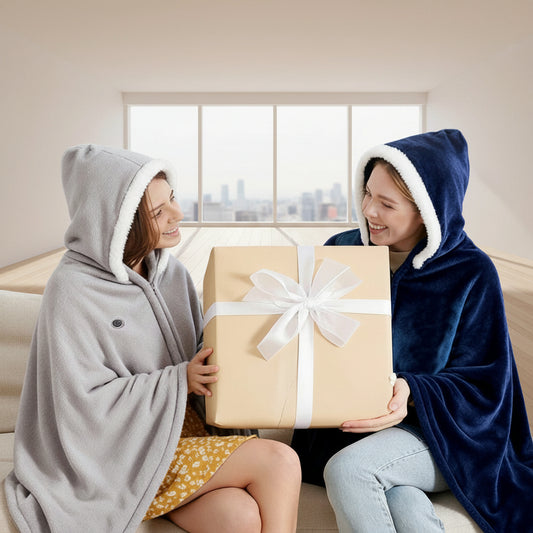 Two people wearing hooded blankets holding a gift box in a cozy living room.